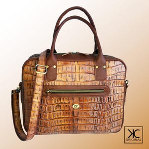 May include: A brown leather briefcase with a crocodile pattern. The bag has a top handle and a long adjustable shoulder strap. The bag has a zipper closure and a front pocket with a zipper.