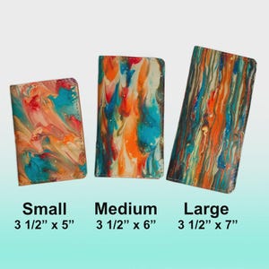 Op de afbeelding: Drie portemonnees met een abstract, kleurrijk patroon in de maten klein, medium en groot. De kleine portemonnee meet 8,9 cm x 12,7 cm, de medium is 8,9 cm x 15,2 cm en de grote is 8,9 cm x 17,8 cm. De portemonnees hebben een marmer effect met blauw, oranje en wit.