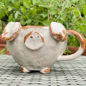 Könnte beinhalten: Eine Keramiktasse in Form eines Schweins mit brauner Glasur. Die Tasse hat einen Henkel und eine Schnauze mit zwei Nasenlöchern.