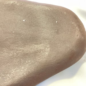 May include: A close-up of a light brown canvas surface with a subtle shimmer. The canvas has a textured weave and appears to be stretched over a frame.