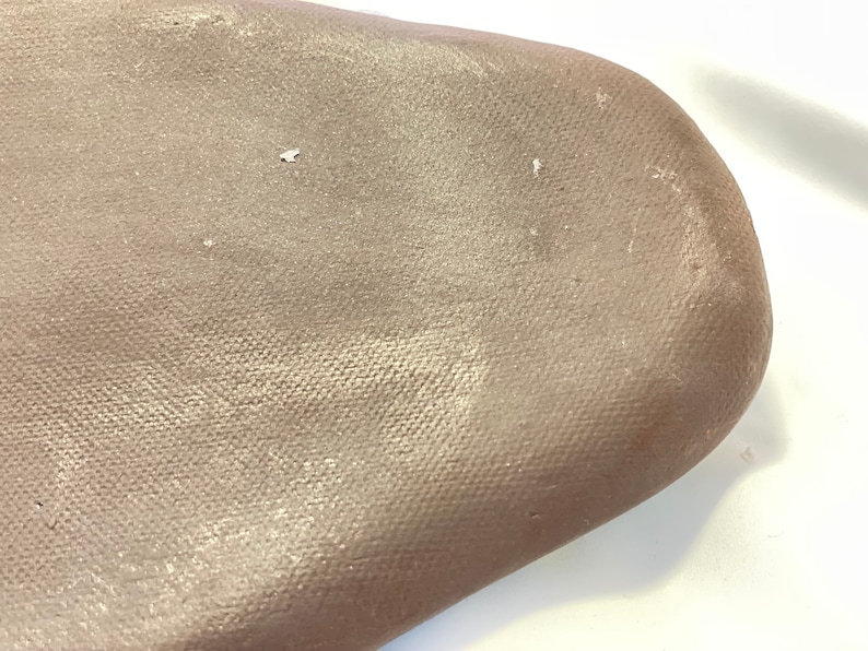 May include: A close-up of a light brown canvas surface with a subtle shimmer. The canvas has a textured weave and appears to be stretched over a frame.
