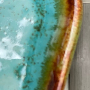 May include: A turquoise, green, and brown ceramic bowl with a glossy finish. The bowl has a unique, organic shape and a slightly raised rim.