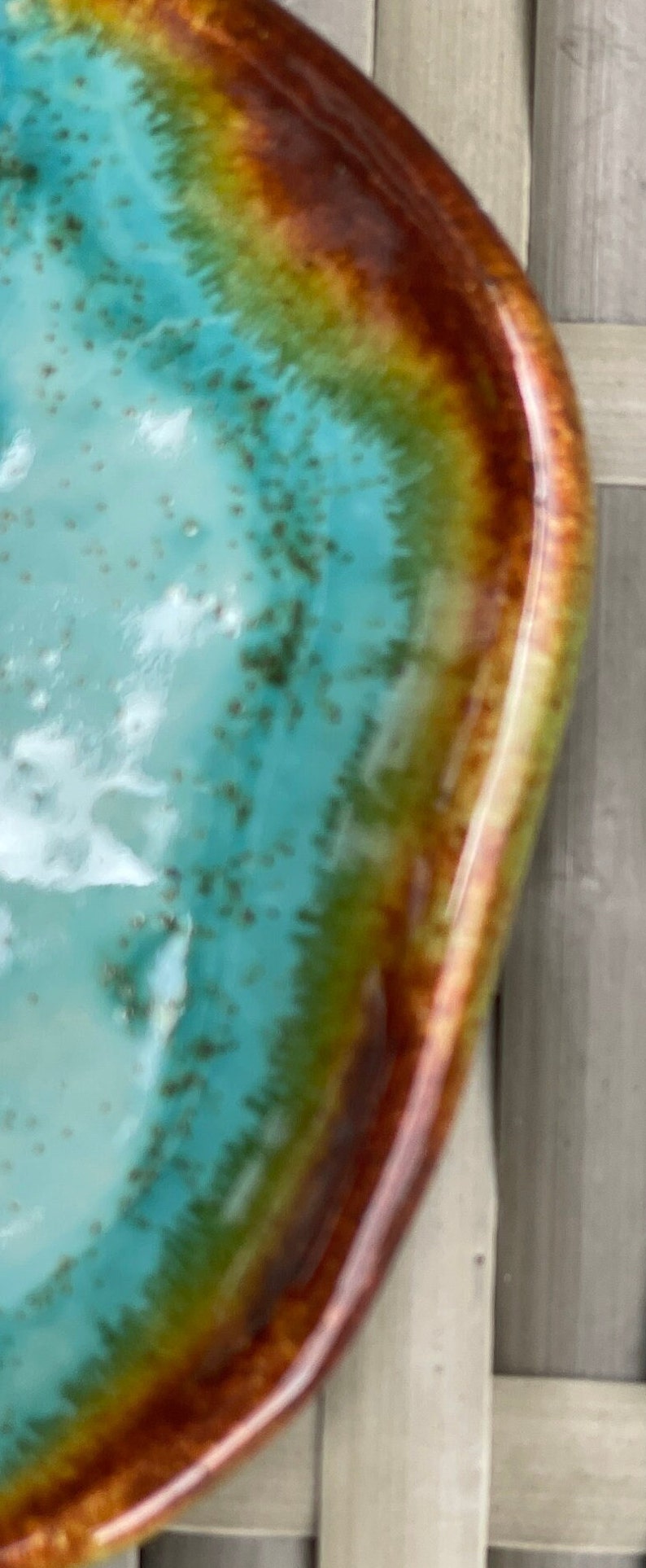May include: A turquoise, green, and brown ceramic bowl with a glossy finish. The bowl has a unique, organic shape and a slightly raised rim.