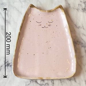 May include: A pink ceramic dish shaped like a cat with a gold rim. The dish is 7.87 inches wide and 8 inches long.