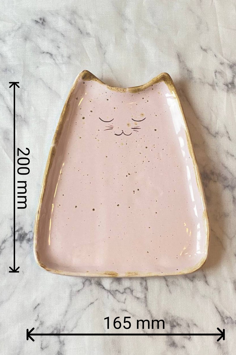 May include: A pink ceramic dish shaped like a cat with a gold rim. The dish is 7.87 inches wide and 8 inches long.