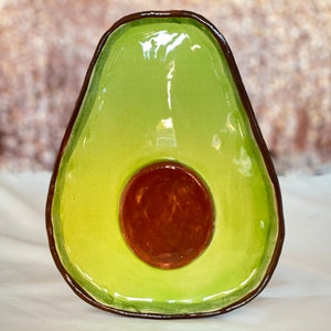 May include: A green ceramic avocado-shaped dish with a brown pit. The dish is glazed and has a glossy finish.