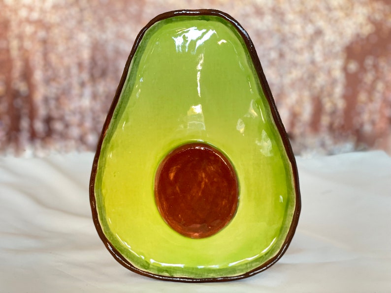 May include: A green ceramic avocado-shaped dish with a brown pit. The dish is glazed and has a glossy finish.