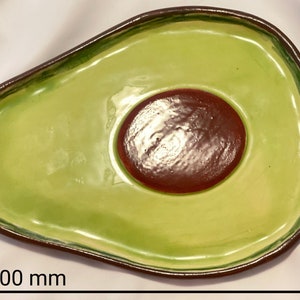 May include: A green ceramic avocado-shaped serving dish with a brown center. The dish measures 8 inches wide and 6.5 inches long.