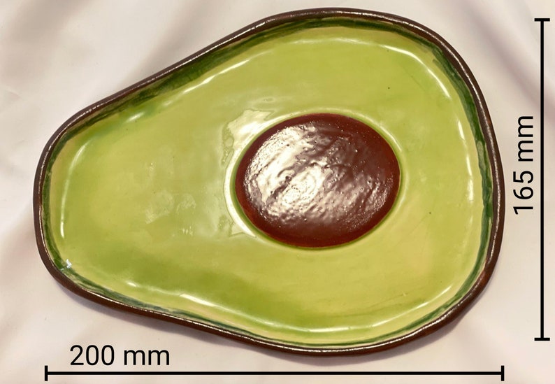 May include: A green ceramic avocado-shaped serving dish with a brown center. The dish measures 8 inches wide and 6.5 inches long.