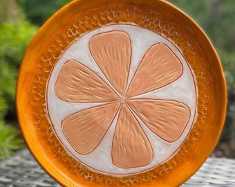 May include: Orange ceramic plate with a raised orange slice design. The plate is a bright orange color with a white center and a raised orange slice design.