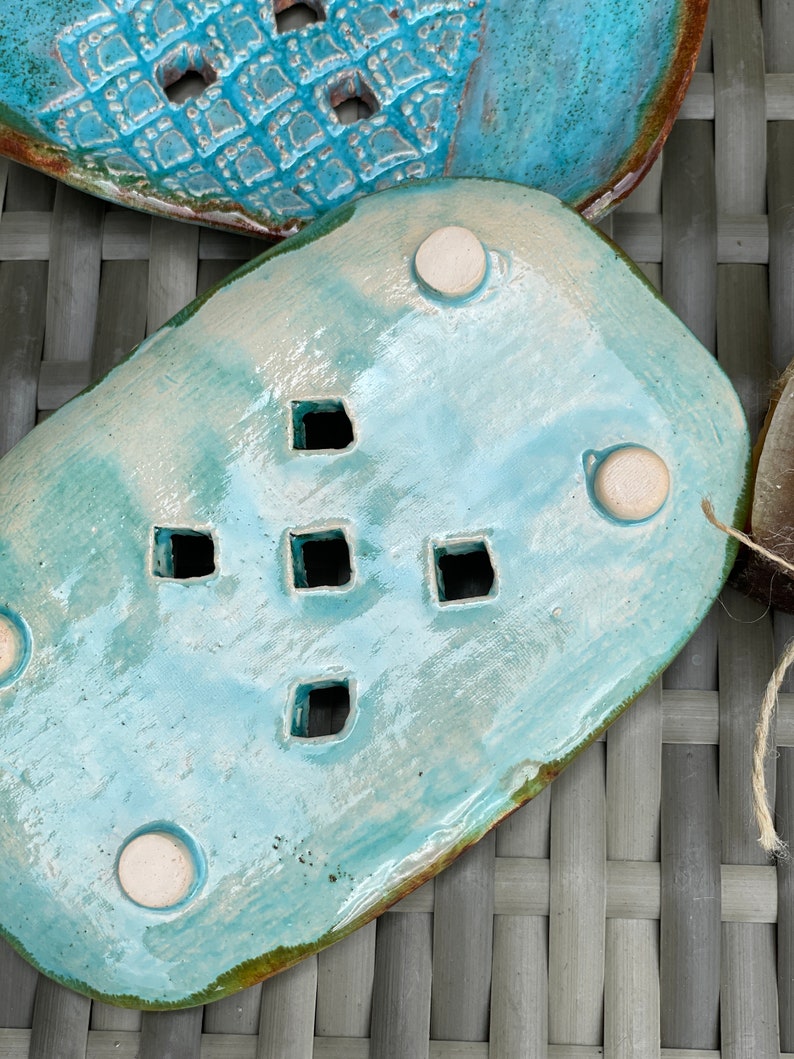 May include: A light blue ceramic soap dish with a decorative design of small squares. The dish has four white feet on the bottom and is designed to drain water.