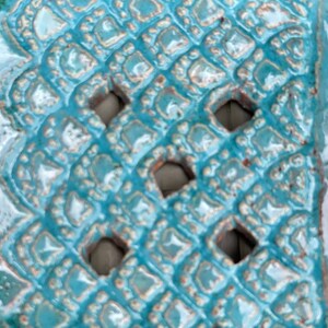 May include: Close-up of a turquoise ceramic tile with a repeating diamond pattern and cut-out holes.