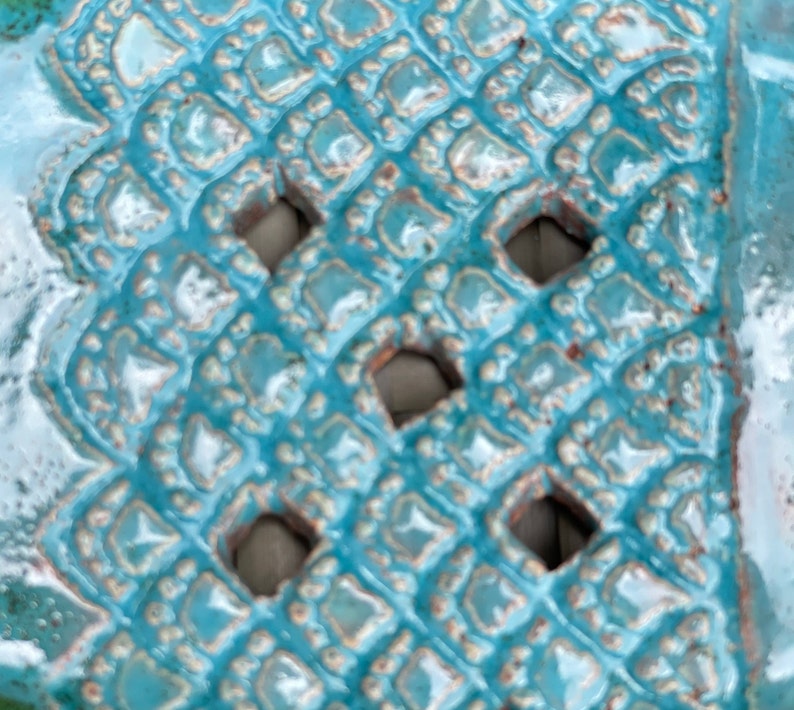 May include: Close-up of a turquoise ceramic tile with a repeating diamond pattern and cut-out holes.