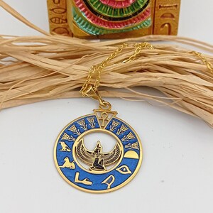 May include: Gold necklace with a blue and gold pendant featuring an Egyptian goddess with outstretched wings. The pendant is surrounded by hieroglyphs and a sun disk.