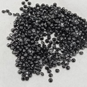 Peut inclure: Un grand tas de strass ronds noirs, &eacute;galement appel&eacute;s cristaux en forme de diamant, sur une surface blanche.