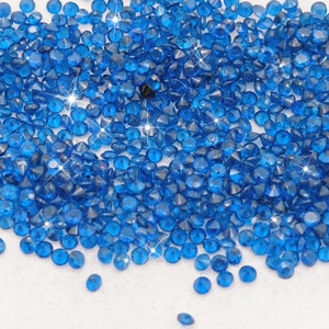 Peut inclure: Un grand tas de petits strass ronds bleus facet&eacute;s. Les strass sont &eacute;parpill&eacute;s sur une surface blanche.