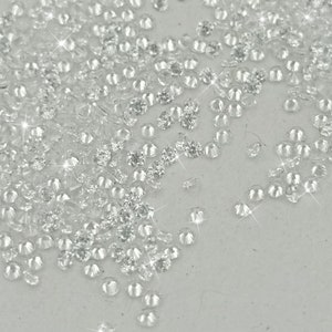 Peut inclure: Une grande quantit&eacute; de petits strass ronds et facett&eacute;s, transparents, &eacute;parpill&eacute;s sur une surface blanche.