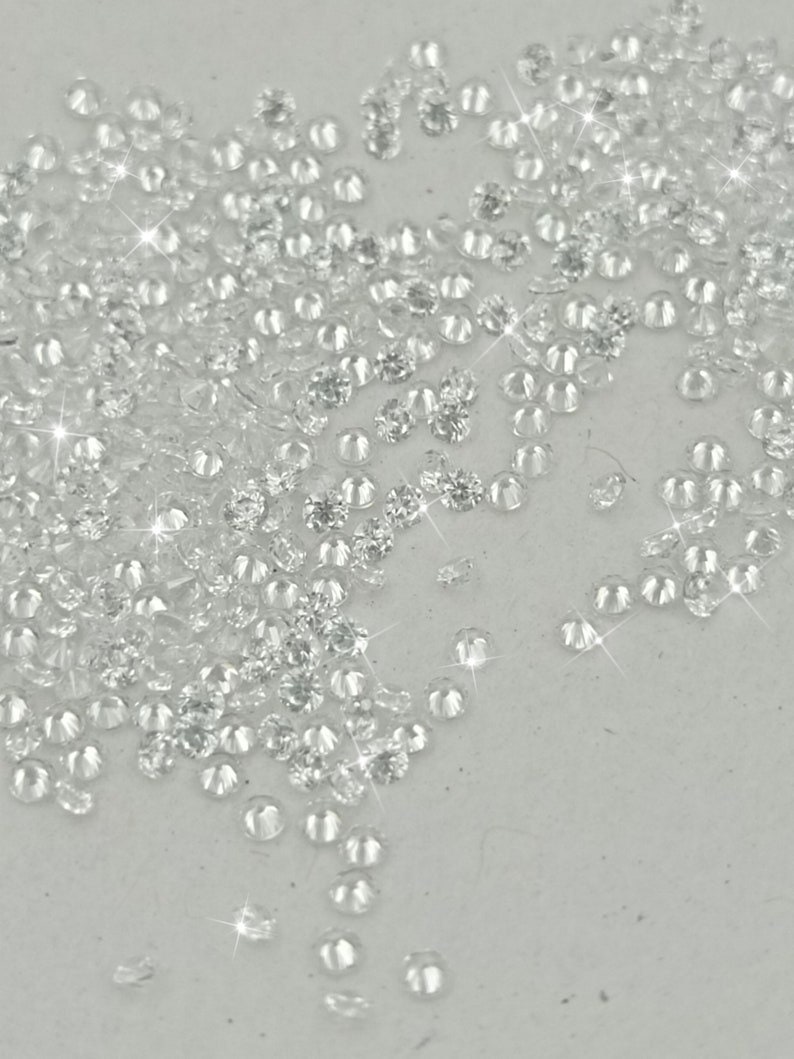 Peut inclure: Une grande quantit&eacute; de petits strass ronds et facett&eacute;s, transparents, &eacute;parpill&eacute;s sur une surface blanche.