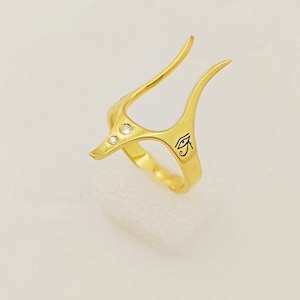 Peut inclure: Bague en or avec un design stylis&eacute; comportant trois petits diamants et un symbole de l'&oelig;il d'Horus grav&eacute;.