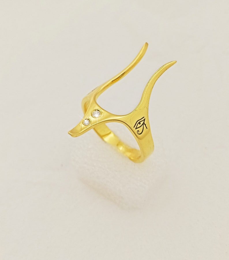 Peut inclure: Bague en or avec un design stylis&eacute; comportant trois petits diamants et un symbole de l'&oelig;il d'Horus grav&eacute;.