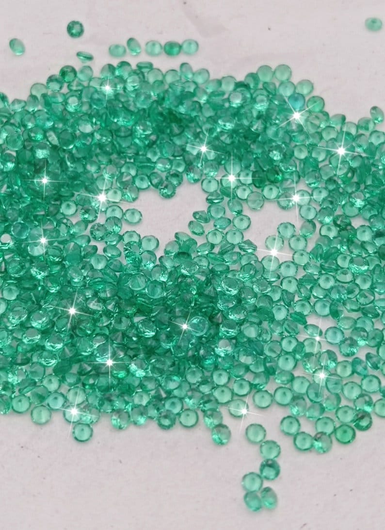 Peut inclure: Une grande quantit&eacute; de petites pierres pr&eacute;cieuses rondes de couleur verte. Les pierres pr&eacute;cieuses sont &eacute;parpill&eacute;es sur une surface blanche.