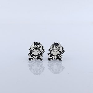 Può includere: Un paio di orecchini a bottone in argento con un personaggio dei cartoni animati in bianco e nero con un'espressione maliziosa.