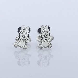 May include: A pair of silver stud earrings featuring a black and white cartoon image of Minnie Mouse.