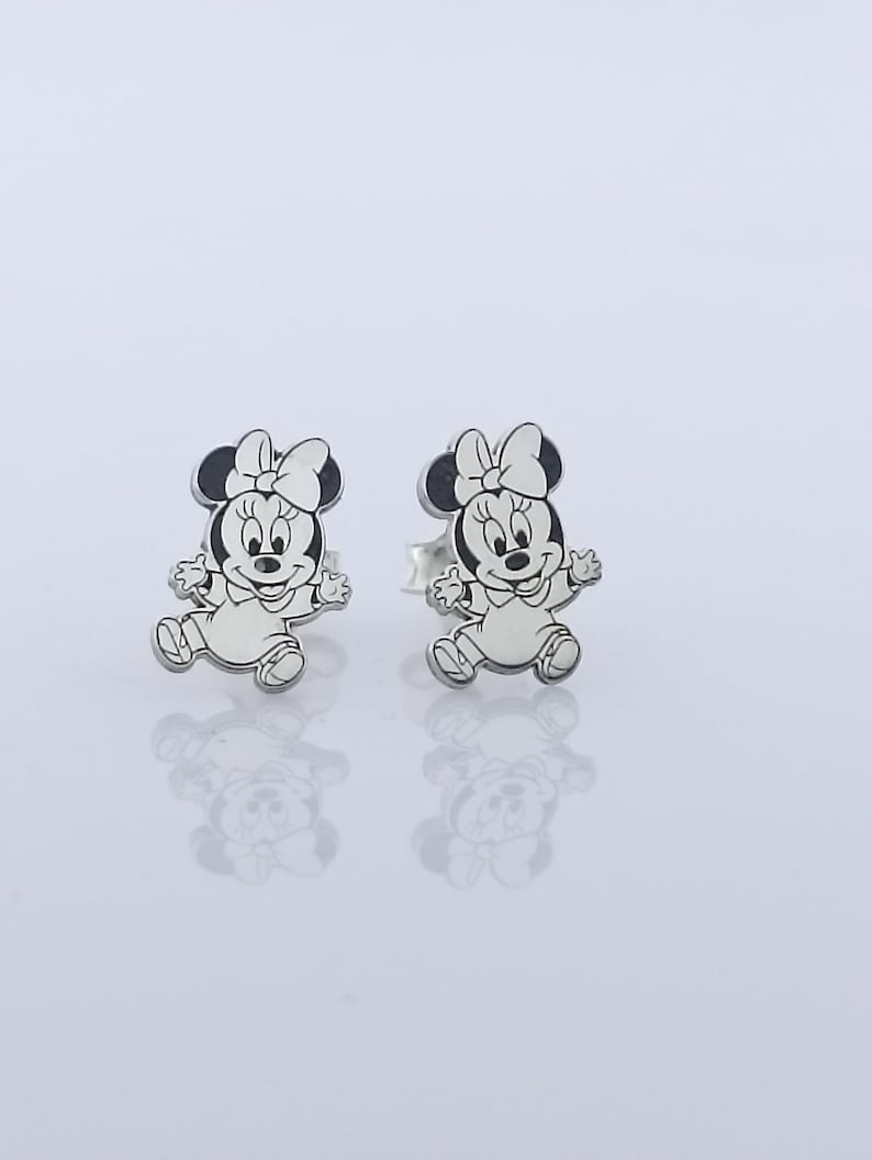 May include: A pair of silver stud earrings featuring a black and white cartoon image of Minnie Mouse.