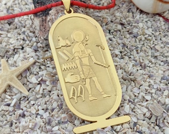 May include: Gold pendant necklace featuring an Egyptian god with a hawk head, standing on a pedestal. The pendant is surrounded by hieroglyphs and symbols.