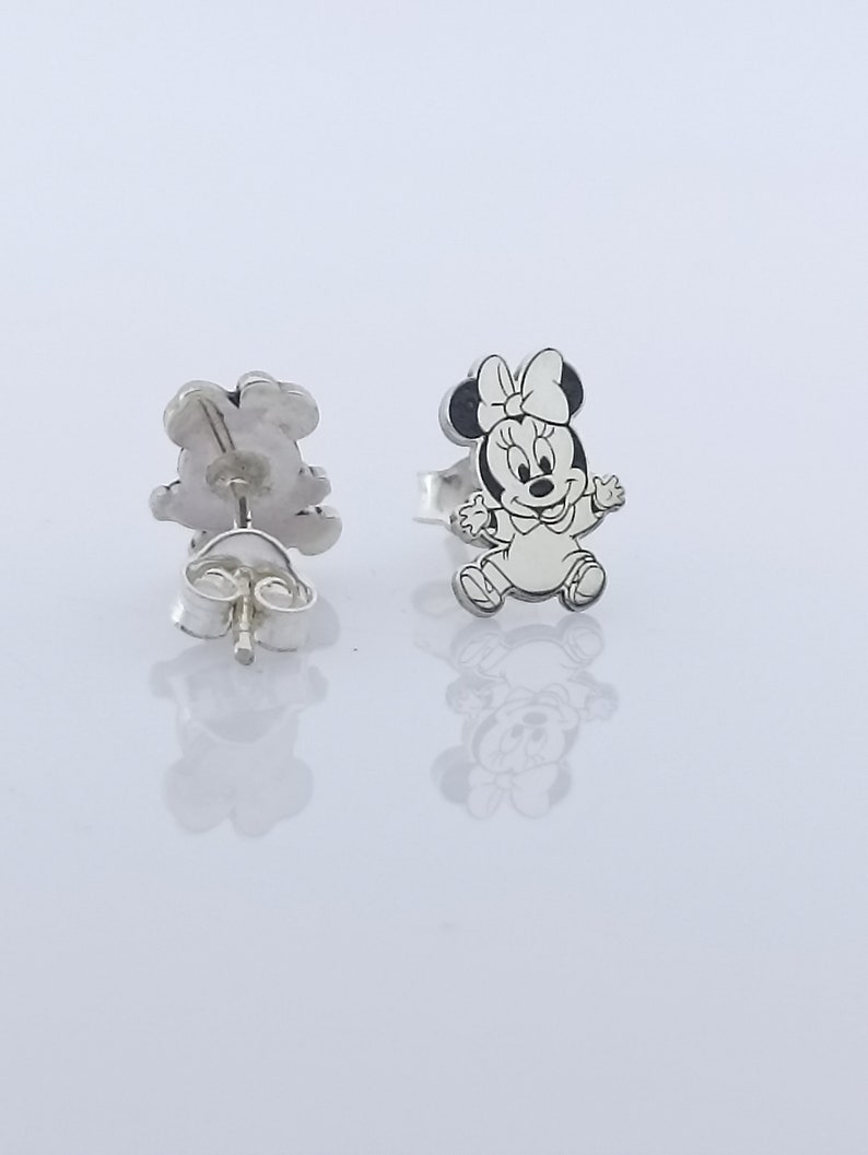 May include: A pair of silver stud earrings featuring a black and white cartoon image of Minnie Mouse. The earrings are designed with a post and butterfly back.