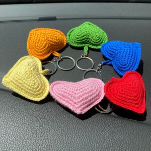 May include: Six crocheted heart-shaped keychains in different colors: yellow, orange, green, blue, pink, and red. The keychains are attached to silver key rings.