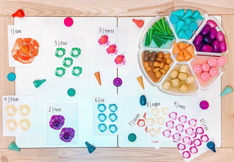 May include: A set of ten colorful cards with numbers 1 through 10 written on them. Each card has a different color and a different number of circles. The circles are painted in different colors. There are also small wooden pieces in different colors and shapes on the table.