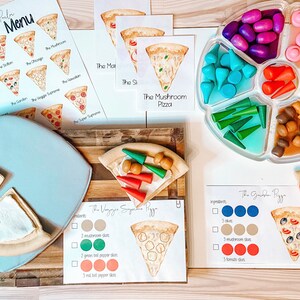 May include: A pizza making play set with a menu, pizza slices, and toppings. The menu includes different pizza options like "The Veggie Supreme" and "The Garden Pizza". The toppings are made of wood and include mushrooms, peppers, and olives.