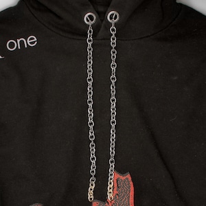 Puede incluir: Sudadera negra con un diseño floral rojo en la parte inferior y la palabra "one" en blanco. La sudadera tiene cordones de cadena plateada.