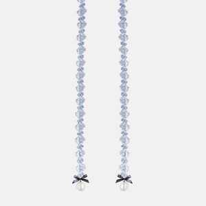 Puede incluir: Un par de cadenas largas y delicadas de plata con abalorios azules en forma de flor y una perla al final de cada cadena. Las cadenas tienen un lazo negro en la parte superior.