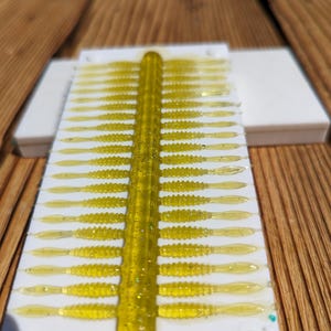 May include: A white plastic mold filled with 24 bright yellow, glitter-infused, soft plastic fishing lures.