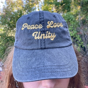 May include: A dark blue denim baseball cap with the words "Peace Love Unity" embroidered in gold on the front.