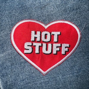 May include: Red heart-shaped patch with a white outline and the text "HOT STUFF" in white letters.