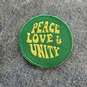 Könnte beinhalten: Ein grüner runder Patch mit gelbem gesticktem Text, der "Peace Love & Unity" lautet.