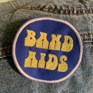 May include: A blue and white embroidered patch with the text "BAND AIDS" in yellow.