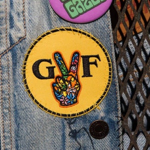 May include: A yellow circular patch with a peace sign and the letters "GVF" in black.