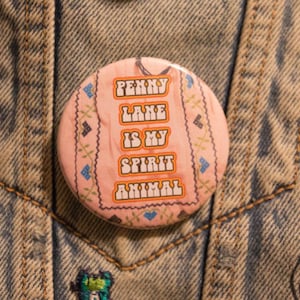 May include: A pink button with a white border and a floral pattern. The text on the button reads "Penny Lane is my spirit animal".