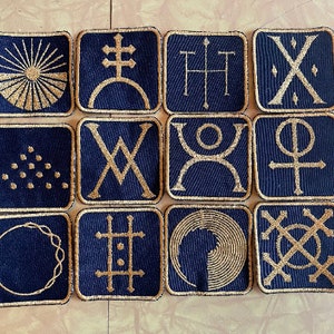 May include: Twelve square patches with gold embroidery on a dark blue background. Each patch features a different geometric design.