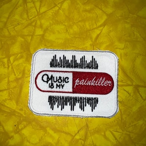 Puede incluir: Parche blanco bordado con ondas sonoras negras y grises. El parche presenta una píldora roja y blanca con el texto "Music is my painkiller" en negro.