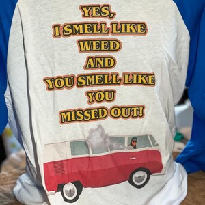 May include: A white and blue baseball t-shirt with the text "YES, I SMELL LIKE WEED AND YOU SMELL LIKE YOU MISSED OUT!" printed on the back. A red and white vintage van with a person driving is printed below the text.