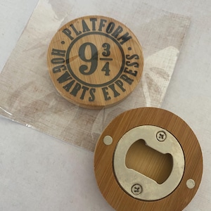Könnte beinhalten: Ein runder Flaschenöffner aus Holz mit einem Metallöffner in der Mitte. Die Oberseite des Flaschenöffners zeigt eine schwarz-weiße Grafik des Hogwarts Express Platform 9 3/4 Logos.