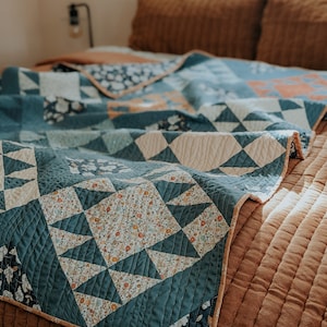 May include: A teal blue and white patterned quilt with a floral design is folded on a brown bed. The quilt has a cream colored border.