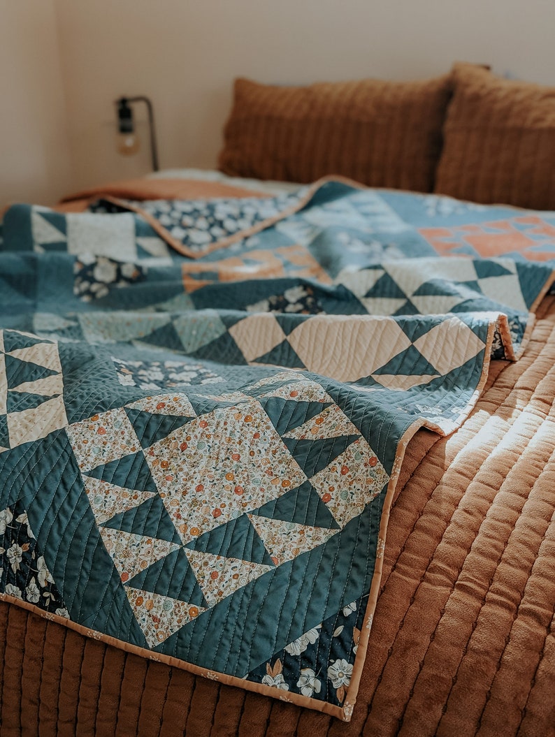 May include: A teal blue and white patterned quilt with a floral design is folded on a brown bed. The quilt has a cream colored border.