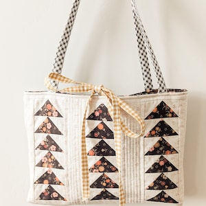 Peut inclure: Un sac cabas matelass&eacute; blanc avec des triangles en tissu noir et floral. Le sac est dot&eacute; d'un ruban jaune et blanc &agrave; carreaux nou&eacute; autour des poign&eacute;es et de sangles en gingham noir et blanc.