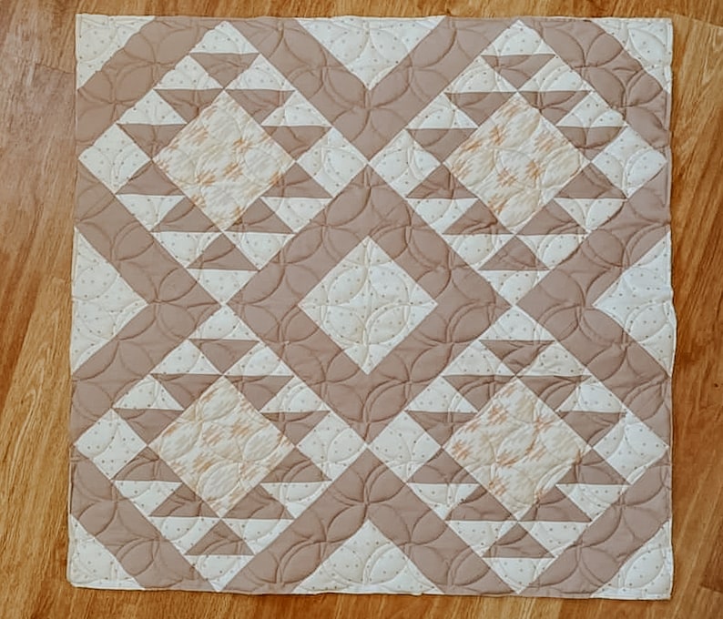 May include: A beige and white quilt with a geometric pattern. The quilt is made of squares and triangles, and the pattern is repeated throughout the quilt.